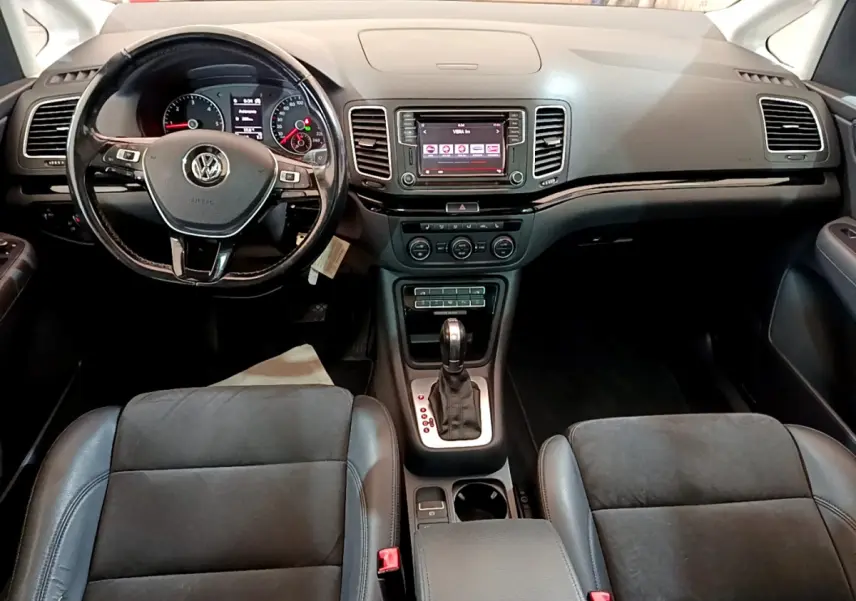 Intérieur noir du Volkswagen Sharan 2017, vue frontale du tableau de bord avec volant multifonctions et écran tactile central.