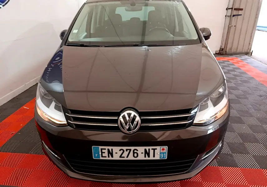 Vue frontale d'un Volkswagen Sharan marron 2017 avec calandre chromée et phares allumés dans un garage.