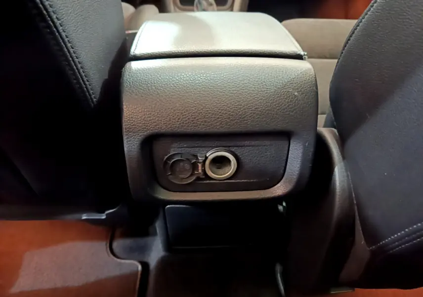 Prise 12V ouverte sous l'accoudoir arrière entre les sièges noirs du Volkswagen Sharan marron 2017.