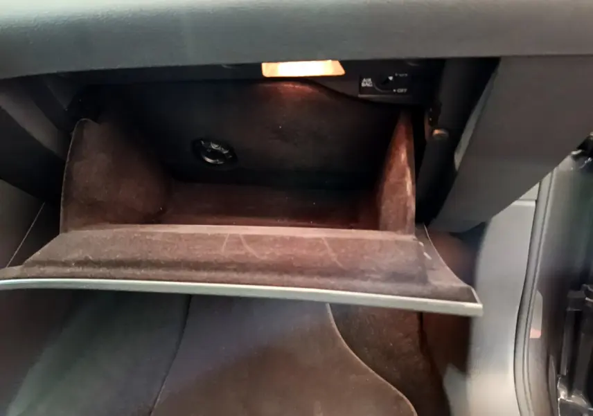 Vue rapprochée de la boîte à gants ouverte du Volkswagen Sharan marron 2017, intérieur sombre et éclairage intérieur allumé.