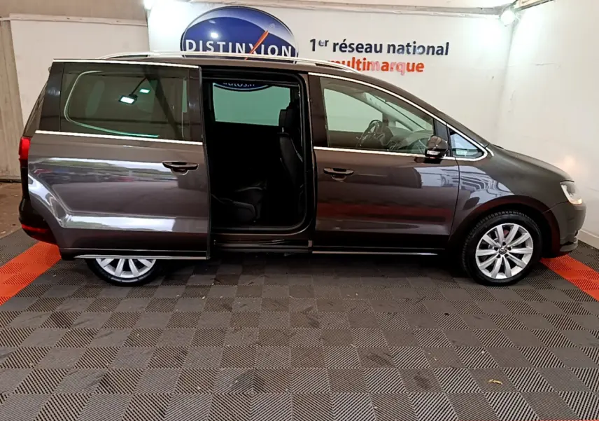 Profil droit d'un Volkswagen Sharan marron 2017 avec porte coulissante arrière ouverte en intérieur showroom.