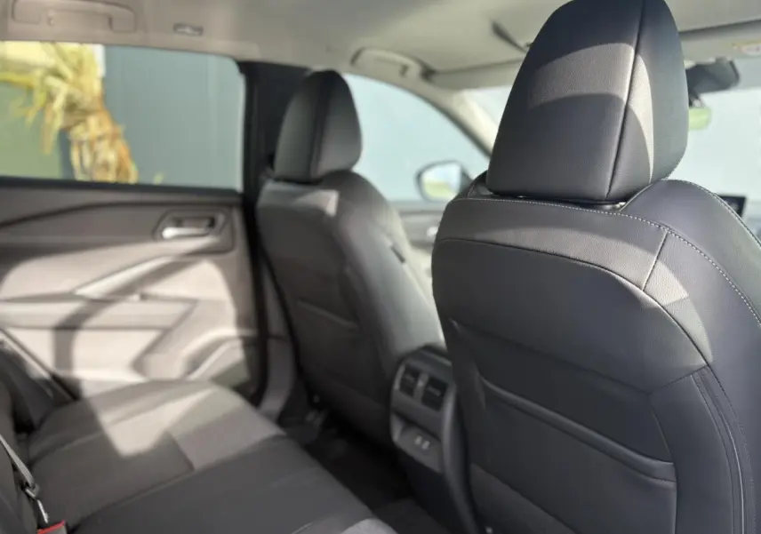 Vue intérieure arrière côté gauche du Nissan Qashqai blanc nacré 2025, montrant les sièges noirs et les aérateurs centraux.