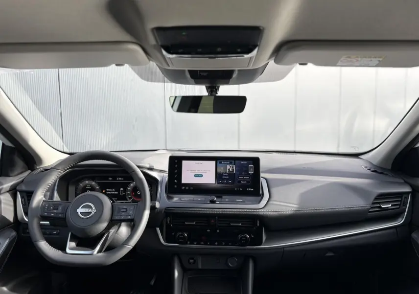 Vue frontale intérieure du Nissan Qashqai blanc nacré 2025, tableau de bord moderne avec écran tactile central et volant multifonction.