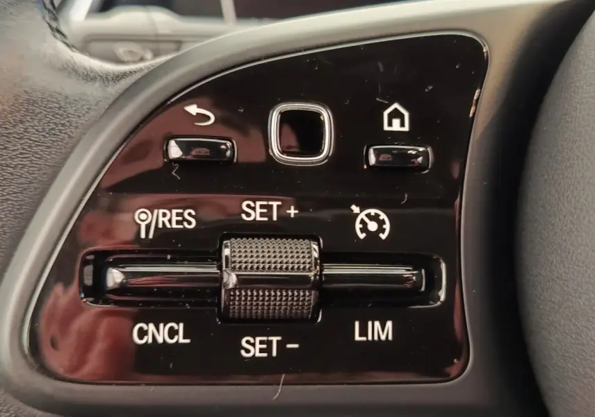 Gros plan sur les commandes de régulateur de vitesse au volant cuir noir de la Mercedes Classe A gris clair.