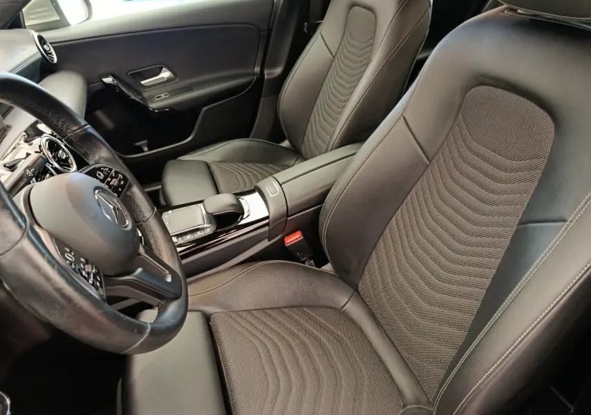 Vue intérieure côté conducteur de la Mercedes Classe A 180 Business Line 2020 avec sièges cuir noirs et volant multifonctions.