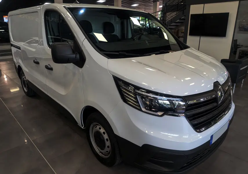 Vue 3/4 avant gauche du Renault Trafic Fourgon blanc minéral 2024 avec calandre noire et phares LED distinctifs.