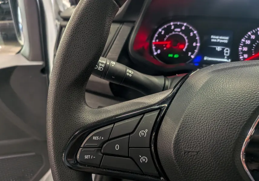 Gros plan sur le volant noir du Renault Trafic Fourgon 2024 avec commandes de régulateur de vitesse et tableau de bord lumineux.