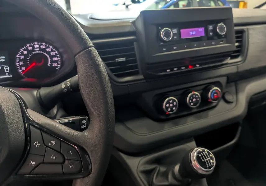 Vue intérieure centrée sur le volant et la console centrale avec levier de vitesse manuel du Renault Trafic Fourgon blanc.