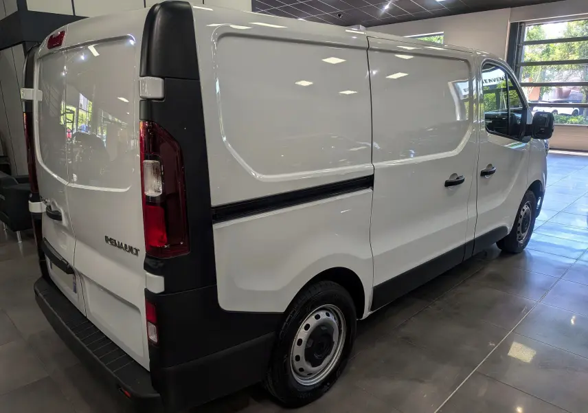 Renault Trafic Fourgon blanc minéral vu en 3/4 arrière droit, avec portes latérales et arrière fermées en intérieur showroom.