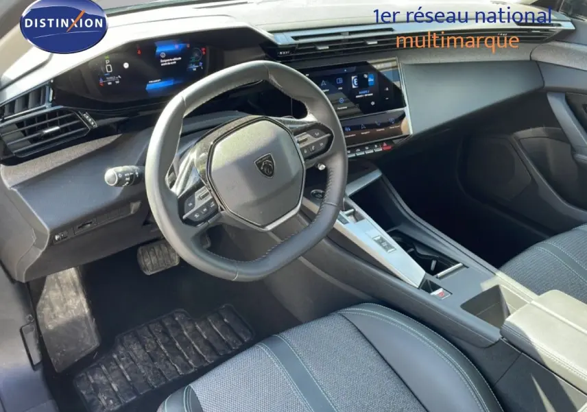 Vue intérieure côté conducteur de la Peugeot 308 SW Hybrid 2025, tableau de bord numérique et volant cuir noir.