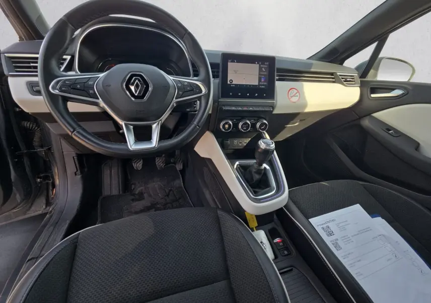 Vue intérieure avant de la Renault Clio V TCE 90 2021, volant multifonction, tableau de bord clair et levier de vitesse manuel.