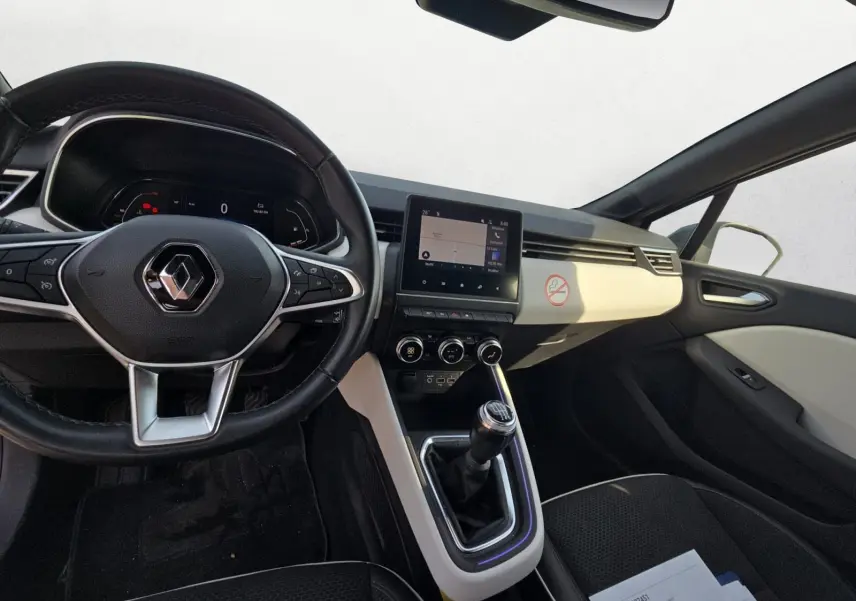 Vue intérieure avant de la Renault Clio V TCE 90 2021, tableau de bord noir et beige avec volant multifonction et boîte manuelle.
