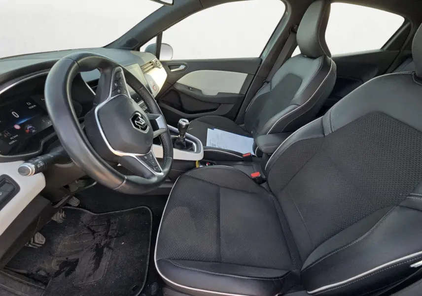 Vue intérieure côté conducteur de la Renault Clio V TCE 90 21 Intens, sièges noirs avec surpiqûres blanches et volant multifonction.