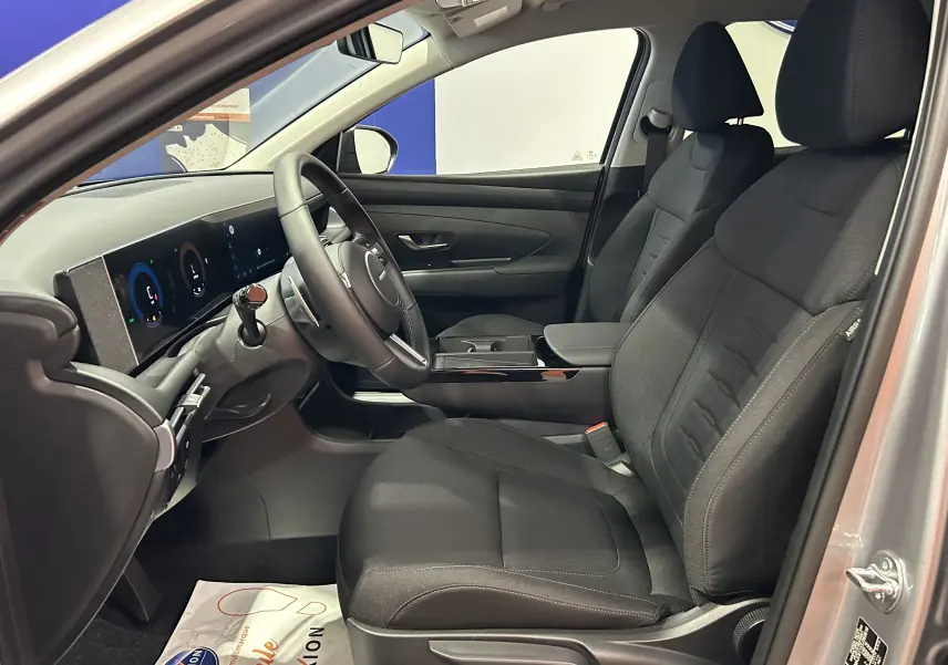 Intérieur avant droit du Hyundai Tucson 2025 gris Shimmering Silver, sièges tissu noirs et tableau de bord numérique.