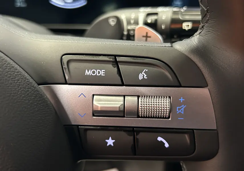 Gros plan sur les commandes gauche du volant du Hyundai Tucson 2025 en cuir noir avec molette et boutons rétroéclairés.