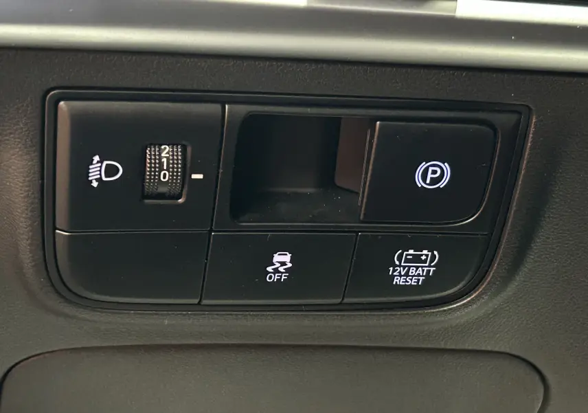 Gros plan sur les commandes de réglage des phares et frein de parking électronique du Hyundai Tucson 2025 intérieur noir.