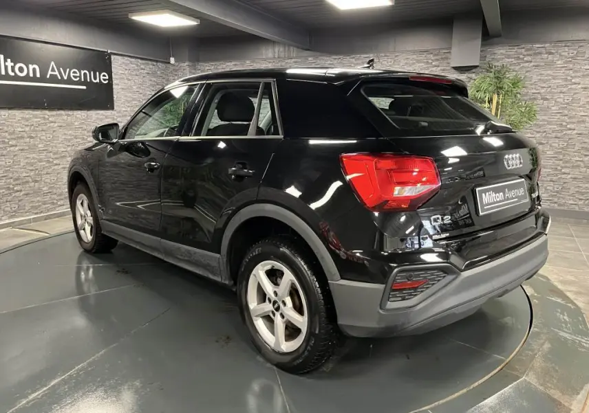 Audi Q2 noir brillant vue 3/4 arrière droit, avec feux LED et jantes aluminium 16 pouces dans showroom.