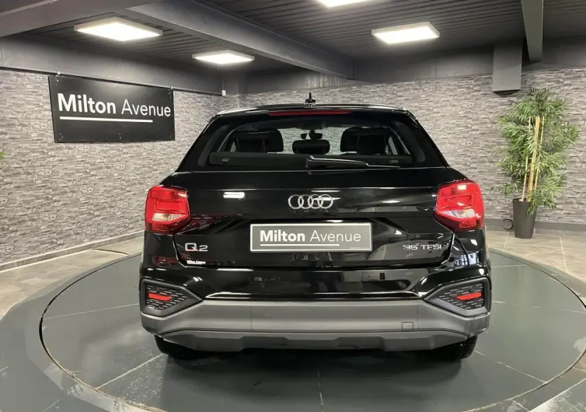 Vue arrière d'un Audi Q2 noir brillant 2022 avec feux LED et logo distinctif sur fond intérieur showroom.