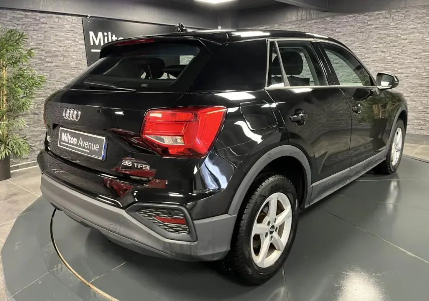 Audi Q2 noir vue 3/4 arrière droit en intérieur, avec feux arrière LED et jantes aluminium 16 pouces.