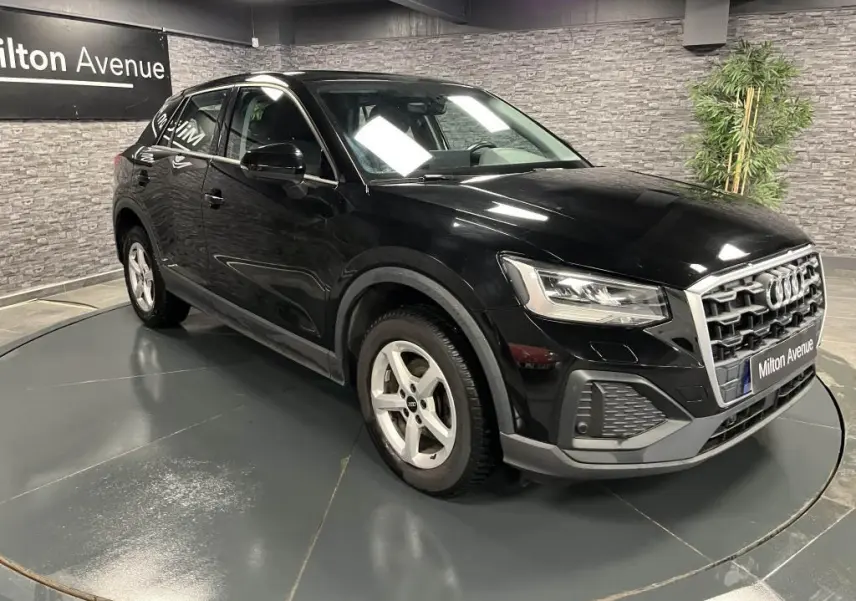 Audi Q2 noir vue 3/4 avant droit avec calandre chromée et jantes aluminium 16 pouces dans un showroom.
