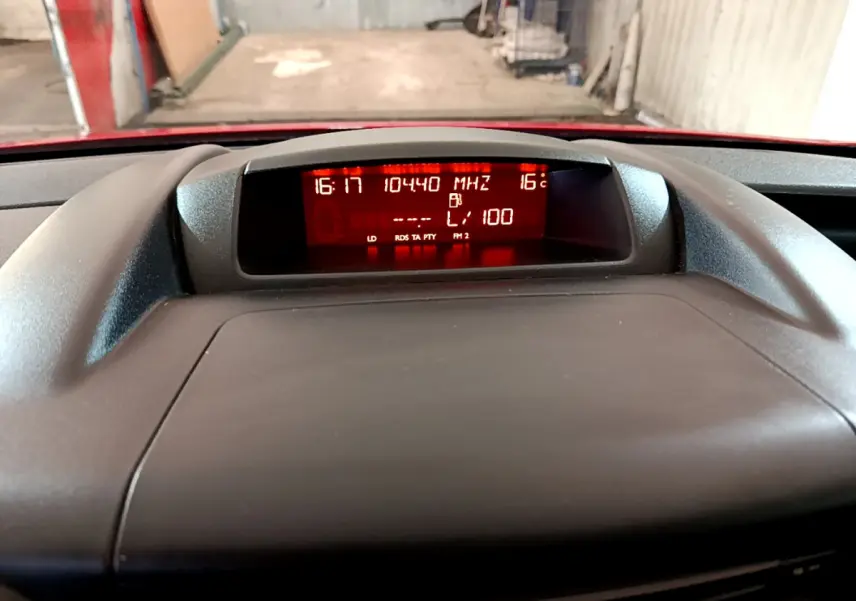 Affichage central du tableau de bord du Citroën Berlingo rouge, montrant l'heure, la température et la fréquence radio.