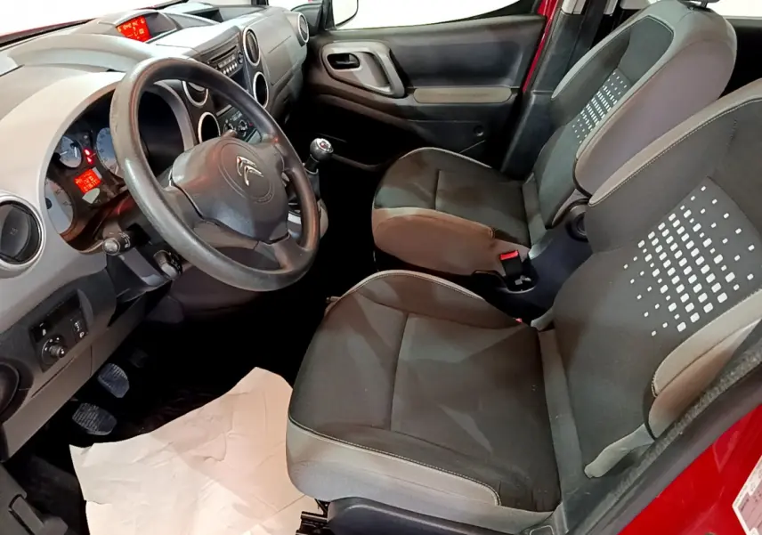 Vue intérieure côté conducteur du Citroën Berlingo rouge 2016, montrant sièges noirs et tableau de bord avec volant.