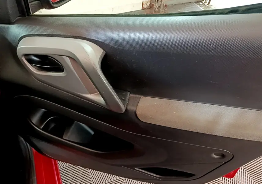 Gros plan sur la porte intérieure côté conducteur du Citroën Berlingo rouge 2016, avec poignée grise et panneau noir.