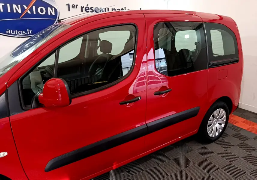 Profil côté gauche du Citroën Berlingo rouge 2016 avec portes vitrées et rétroviseurs assortis en intérieur showroom.