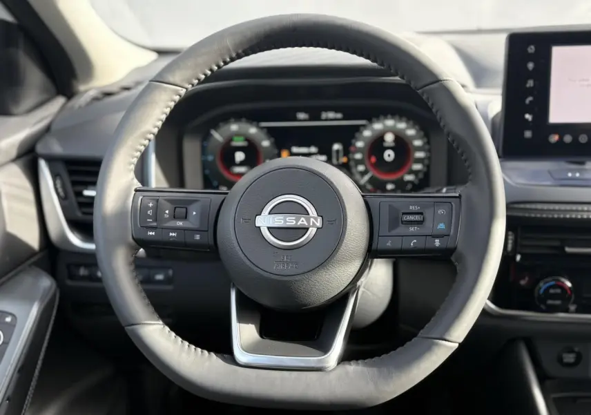 Vue frontale du volant cuir noir du Nissan Qashqai blanc nacré 2025 avec commandes intégrées et tableau de bord numérique.