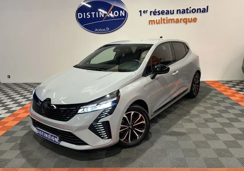 Renault Clio V E-Tech gris Rafale métal en 3/4 avant droit, phares LED allumés et jantes noires bicolores.