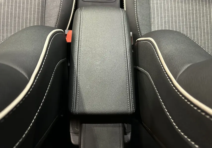 Vue rapprochée de l'accoudoir central en cuir noir avec surpiqûres blanches entre les sièges avant gris de la Renault Clio V.