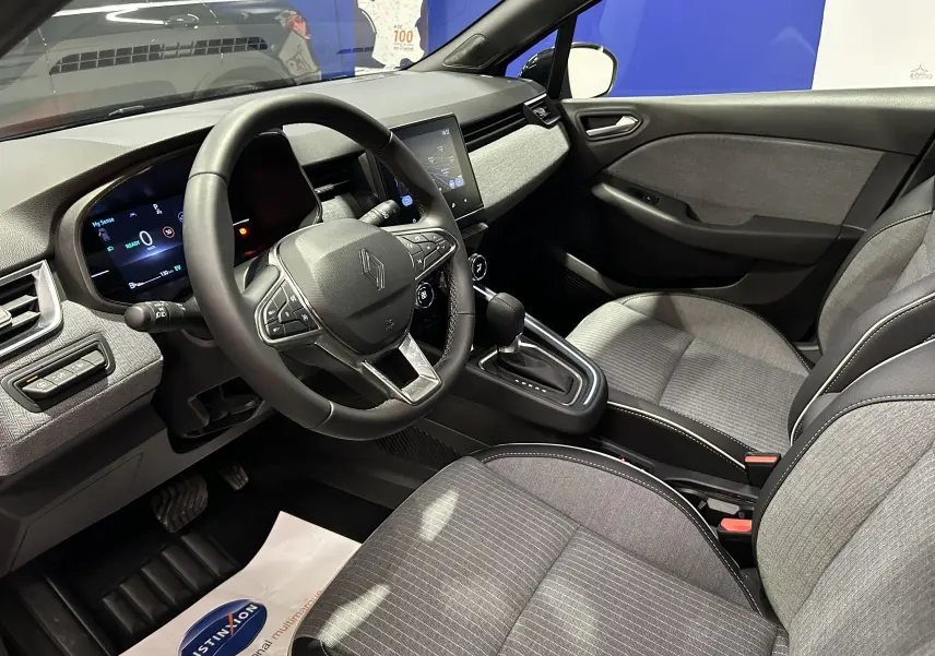 Vue intérieure côté conducteur de la Renault Clio V E-Tech 145ch gris Rafale, avec volant multifonction et écran tactile central.