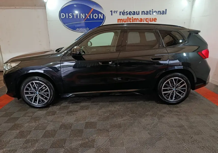 BMW X1 xDrive23i M Sport noir vue de profil côté gauche, avec jantes alliage et vitres teintées en intérieur showroom.
