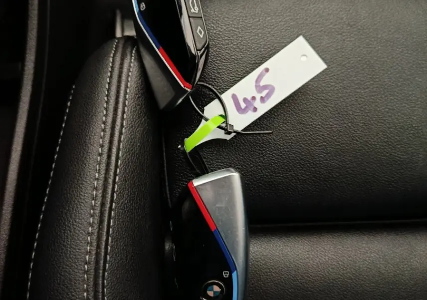 Gros plan sur deux clés BMW noires avec bandes tricolores posées sur un siège en cuir noir.