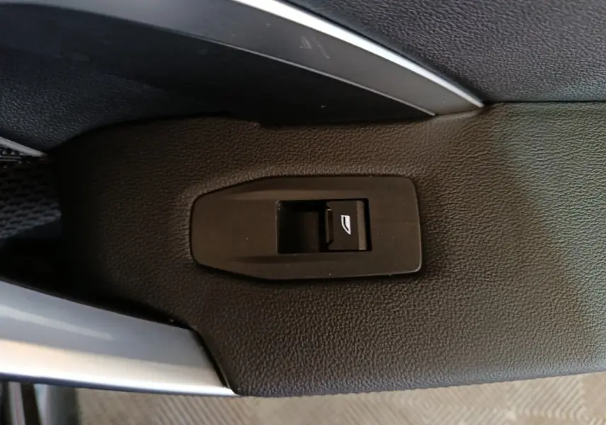 Gros plan sur le bouton de commande de lève-vitre arrière sur la porte intérieure noire d’un BMW X1 xDrive23i M Sport 2023.