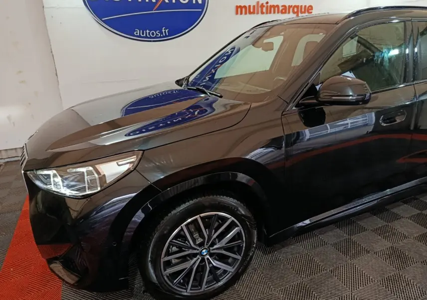 Vue 3/4 avant gauche d’un BMW X1 xDrive23i M Sport noir brillant avec jantes alliage et phares LED visibles.