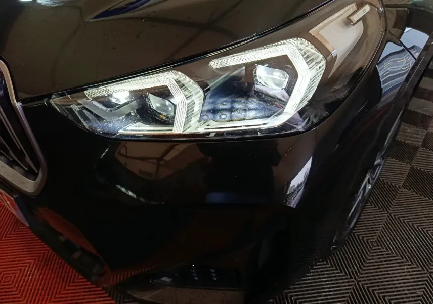 Gros plan sur le phare avant droit LED d’un BMW X1 noir xDrive23i M Sport 2023, avec calandre partielle visible.