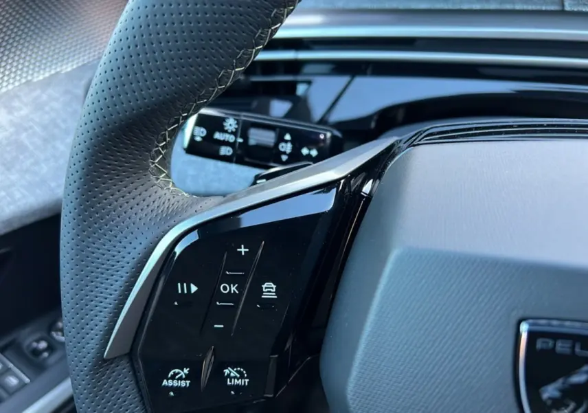 Gros plan sur le volant cuir perforé de la Peugeot 3008 Hybrid 145 GT, avec commandes multifonctions noires brillantes.