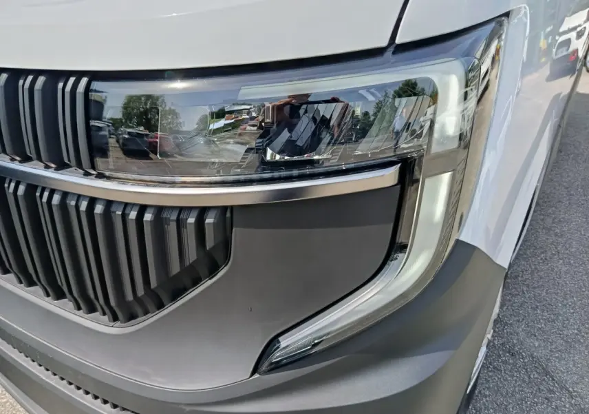 Gros plan sur le phare avant droit et la calandre noire du Renault Master blanc, avec détails modernes et finition mate.