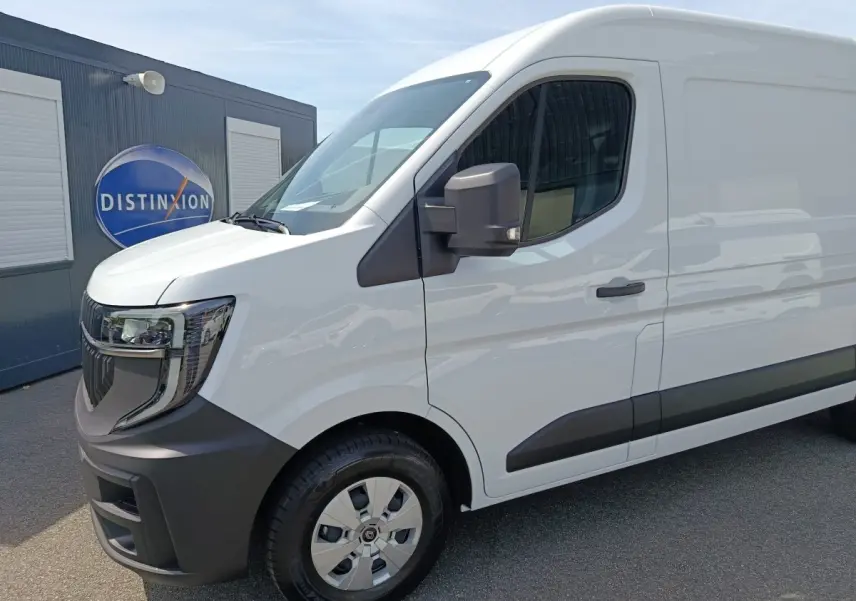 Vue 3/4 avant droit d’un Renault Master blanc avec pare-chocs noirs et rétroviseur noir, stationné devant un bâtiment.