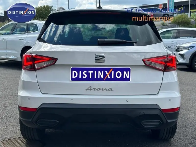 Vue arrière d'un SEAT Arona blanc Nevada avec toit noir, feux LED et logo distinctif sur parking.