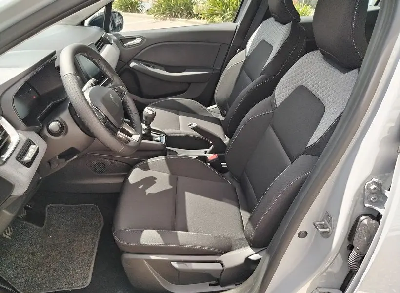 Vue intérieure côté conducteur de la Renault Clio V TCE 90 Evolution 2026, sièges tissu noir et gris, volant multifonction et levier de vitesse manuel.