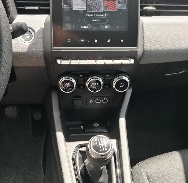 Vue intérieure centrée sur la console centrale de la Renault Clio V TCE 90 Evolution, avec écran tactile et levier de vitesse manuel.