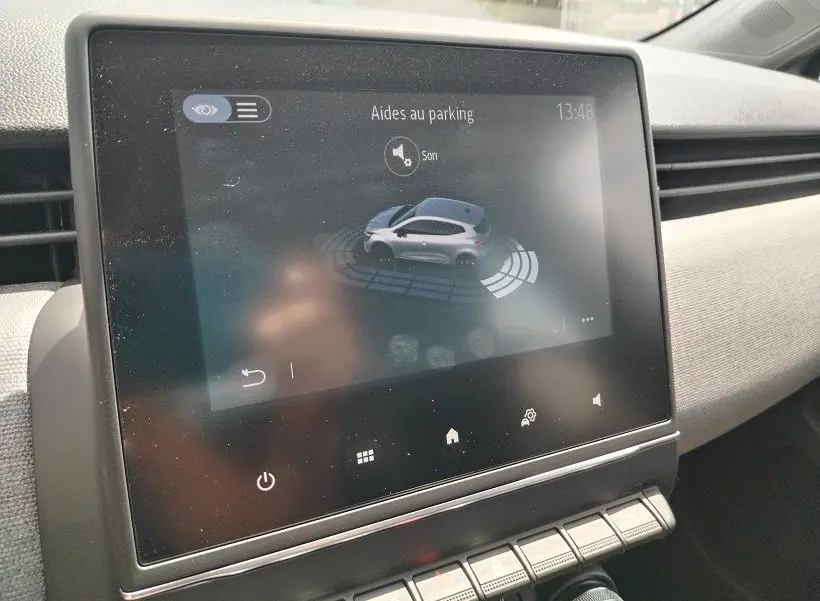 Écran tactile intérieur montrant l'aide au parking de la Renault Clio V gris Rafale, vue de face du tableau de bord.