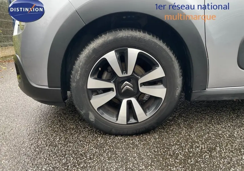Gros plan sur la roue avant gauche d'une Citroën C3 gris acier métal avec jante alliage bicolore et logo Citroën central.