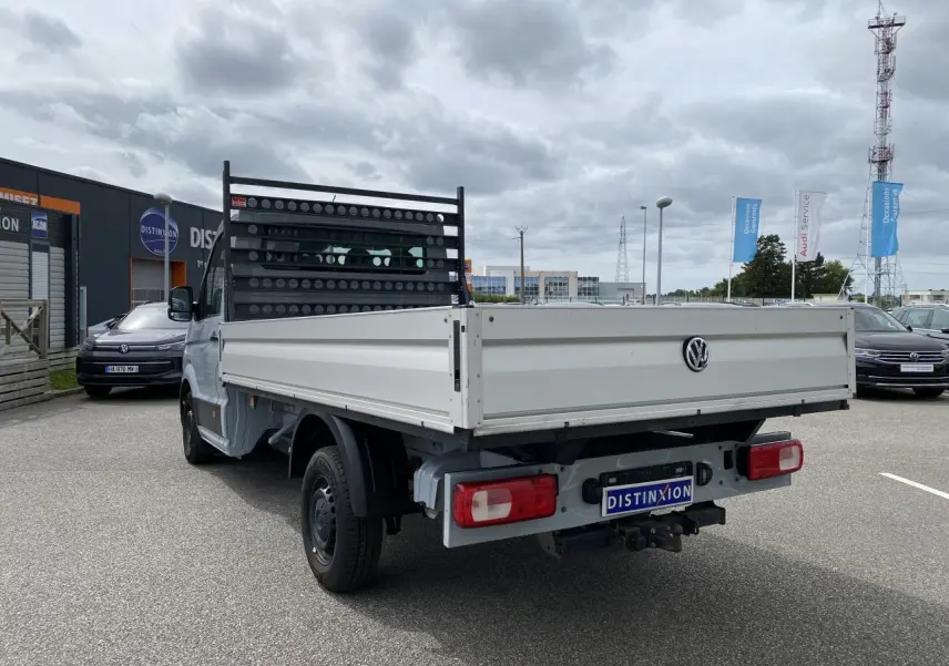 Vue 3/4 arrière droite d'un Volkswagen Crafter fourgon gris argent avec plateau et dispositif d'attelage rigide visible.