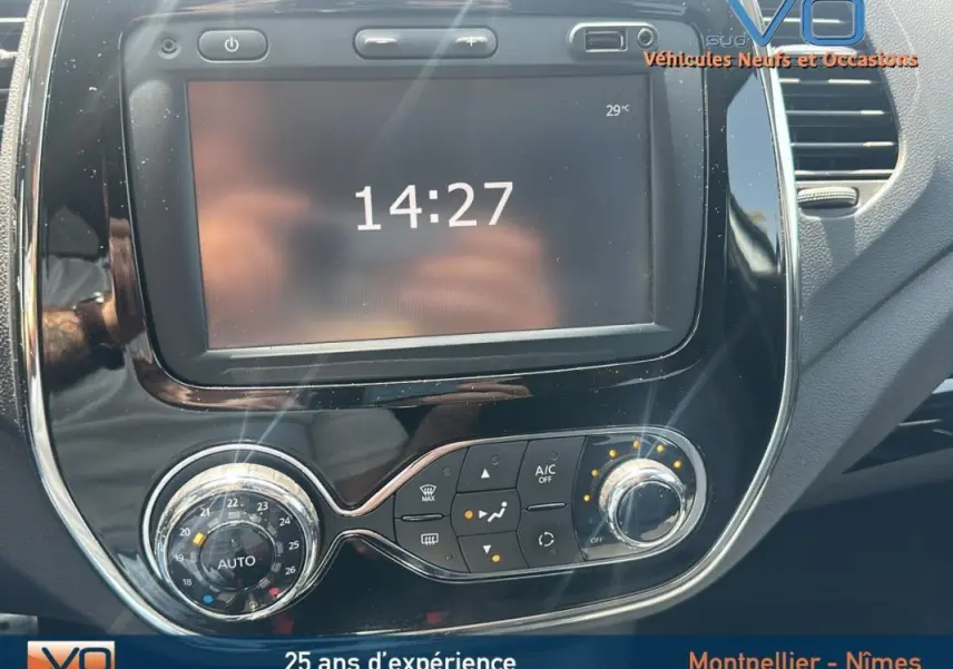 Gros plan sur la console centrale noire brillante du Renault Captur gris clair, affichant l'heure et les commandes de climatisation.