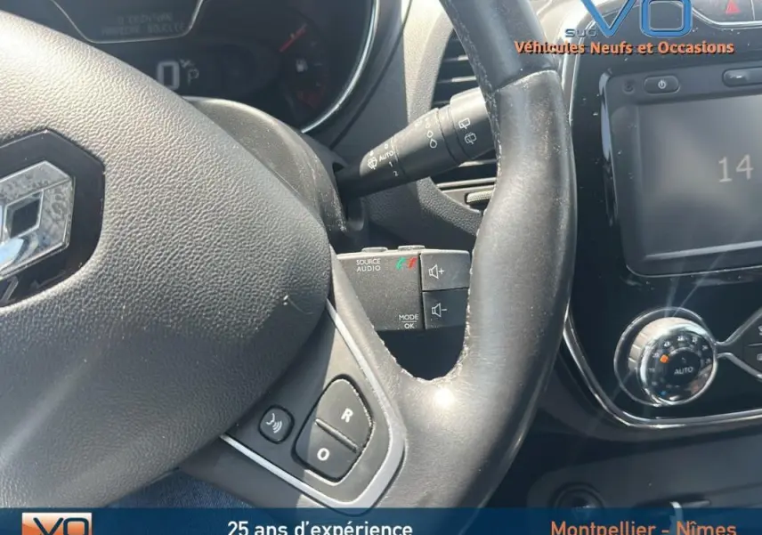 Gros plan sur le volant cuir et la console centrale du Renault Captur gris clair, mettant en valeur les commandes audio et climatisation manuelle.