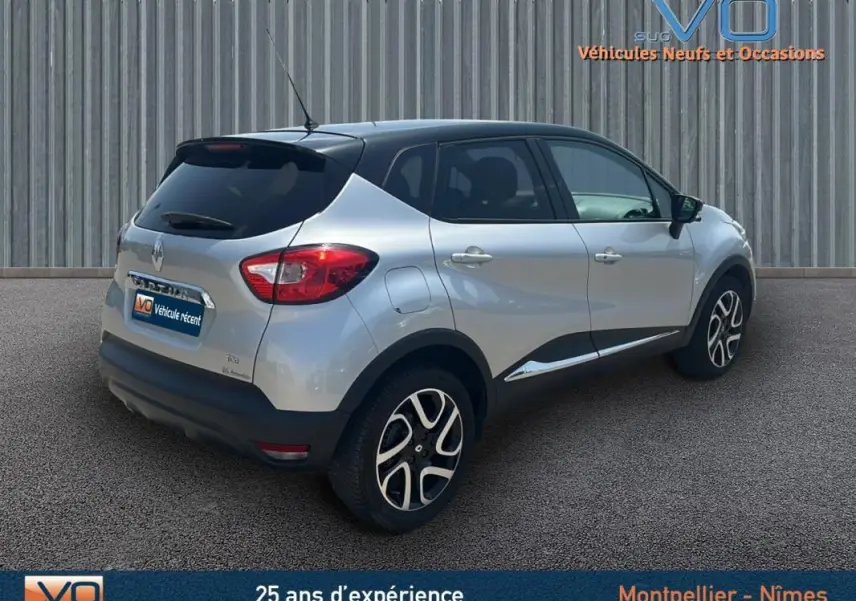 Vue 3/4 arrière droite d'un Renault Captur gris clair avec jantes alliage et toit noir sur fond industriel.