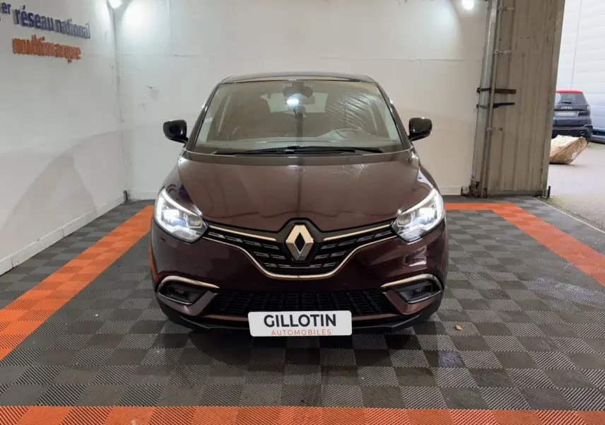 Renault Scénic Intens rouge vue de face avec phares allumés dans un garage au sol damier noir et orange